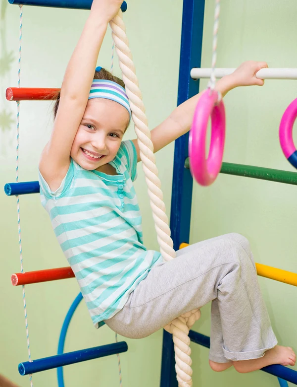 A young girl hanging on a rope and bars on indoor jungle gym.