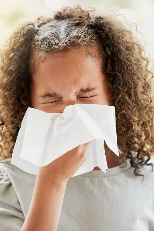 Girl sneezing with eyes closed tightly and tissue on her nose.