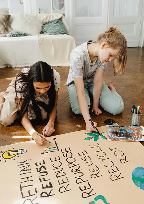 Girls writing on eco awareness poster on the floor.