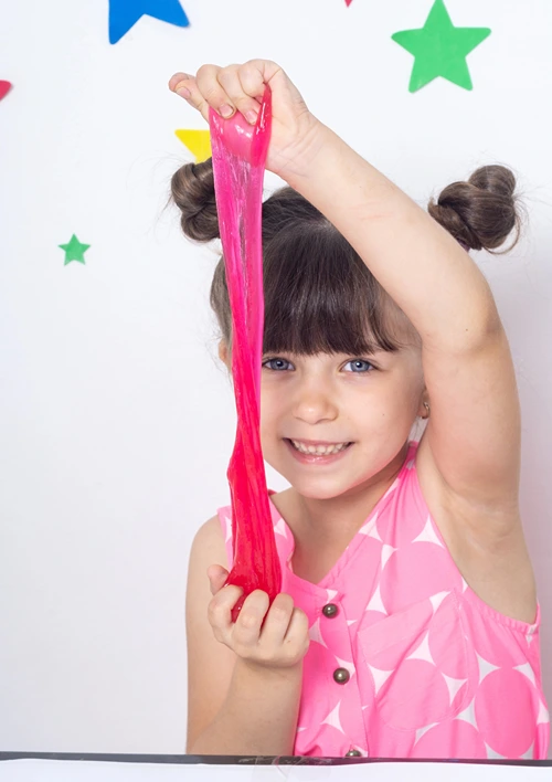 A little girl holding up slime and stretching it.
