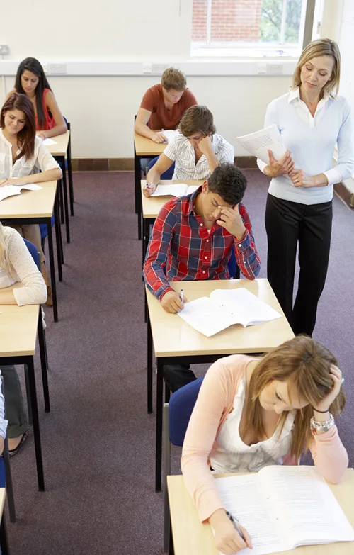 Class of teen students take exam as teach walks the isles