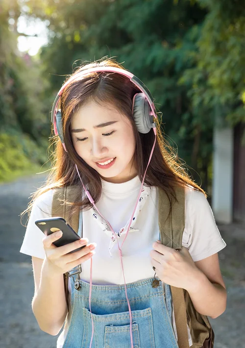 female teen with walking with headphones and smiling at her smartphone.