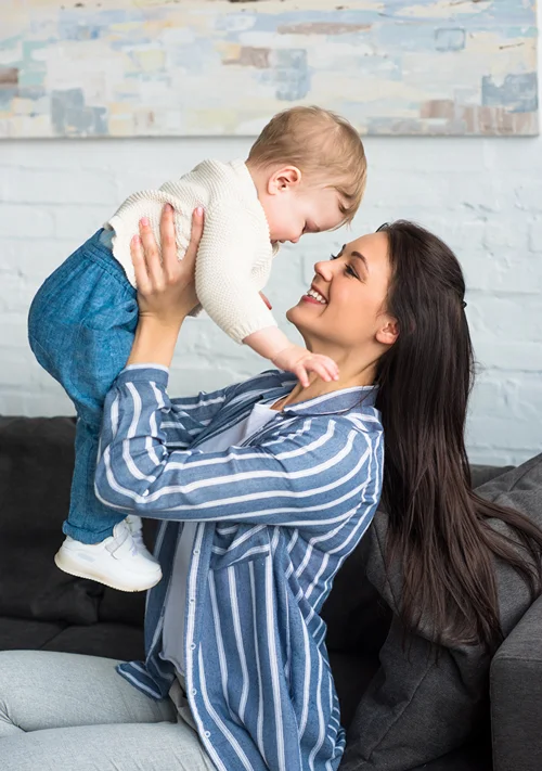 Smiling woman holding up happy toddler.