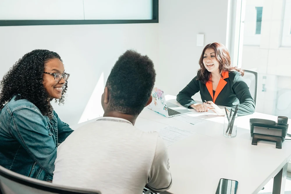 A smiling support worker is meeting in her office with a couple.