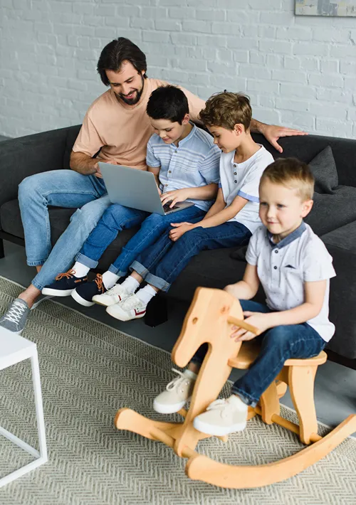 A boy watching TV while dad and brothers play on laptop.