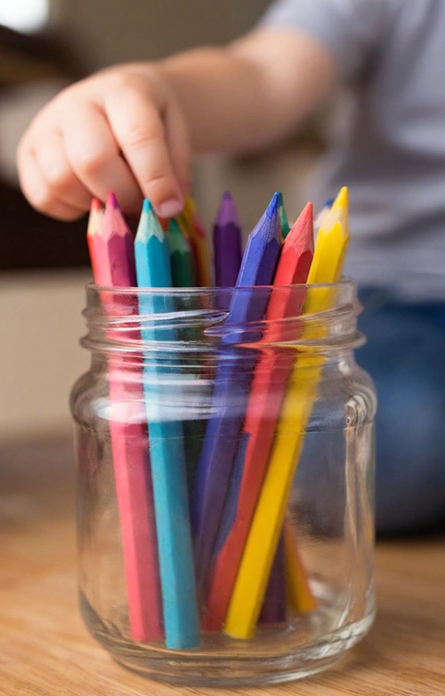 Hand of a boy picks a pencil crayon from a jar.