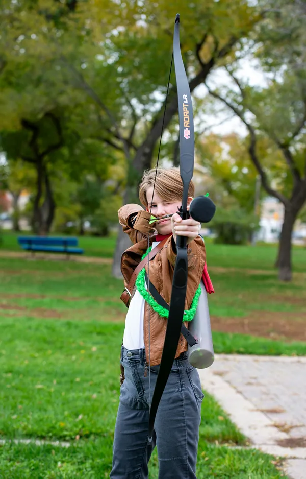 Teen girl in a park stands ready with bow and arrow.
