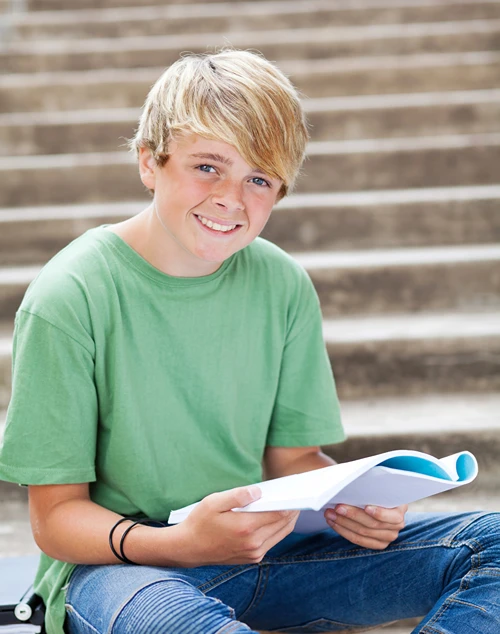 A boy is sitting on school steps outside with an open notebook.
