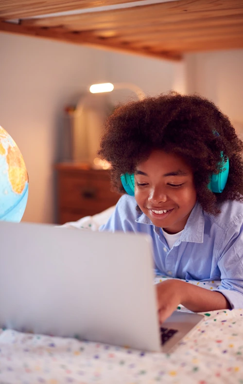 A young girl on her bed is typing on a laptop.
