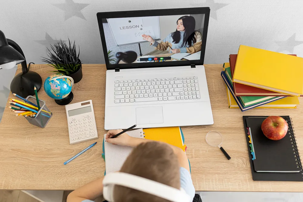 A middle school aged student is sitting at a desk and taking notes during online class.