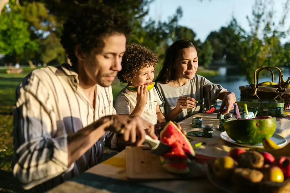 A family eating watermelon outside at a picnic table.