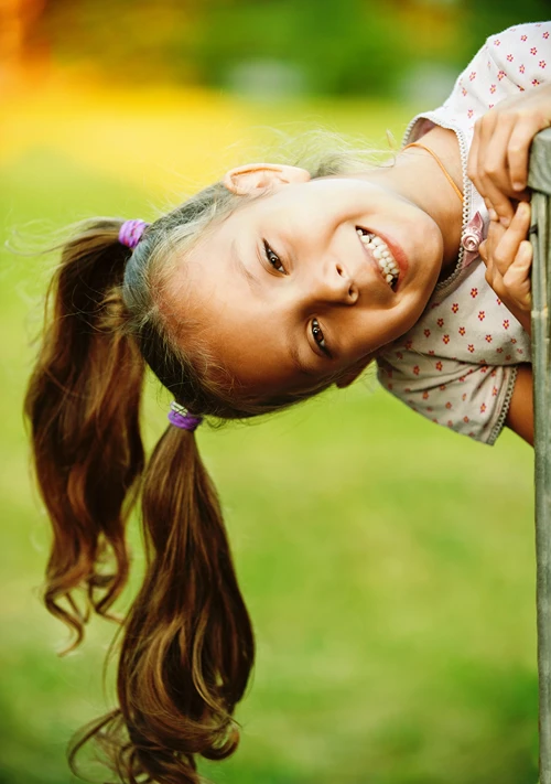 A girl outdoors with big smile as she hangs sideways while playing.