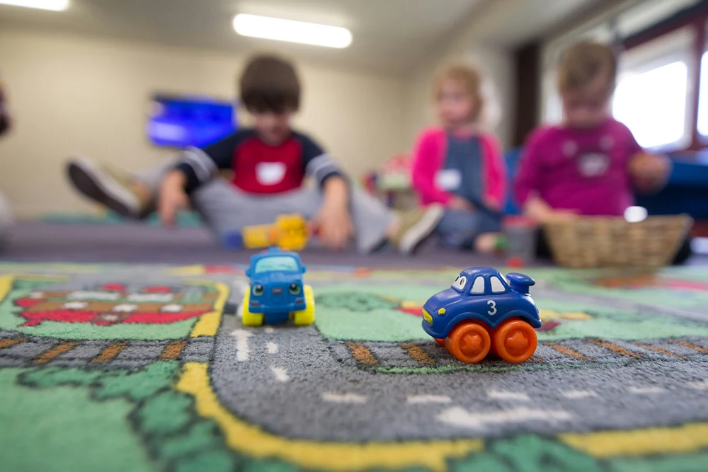 Closeup of toys on a play rub with pre-school child blurred in the background.