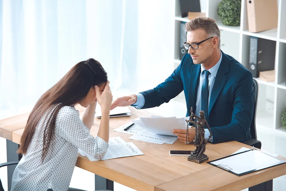 Distressed woman looks down at paper during meeting with a lawyer.