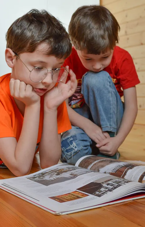 Two boys lay on the floor reading a picture book.
