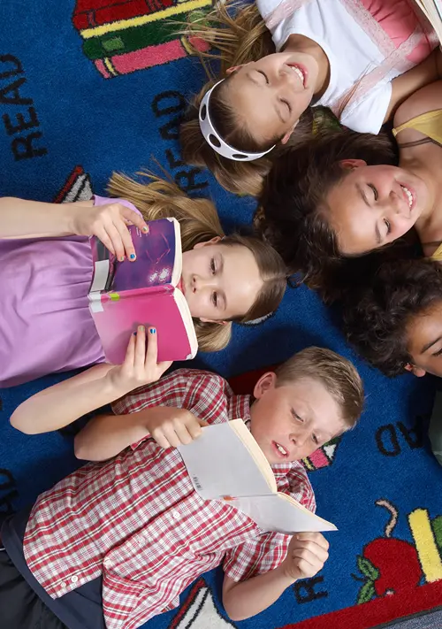 Group of kids laying on their backs on the floor and reading books.