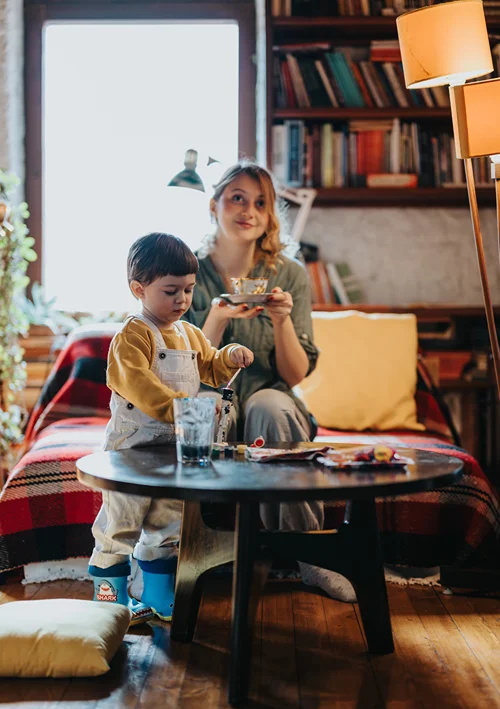Mom smiling with her cup of coffee while child plays at the coffee table.