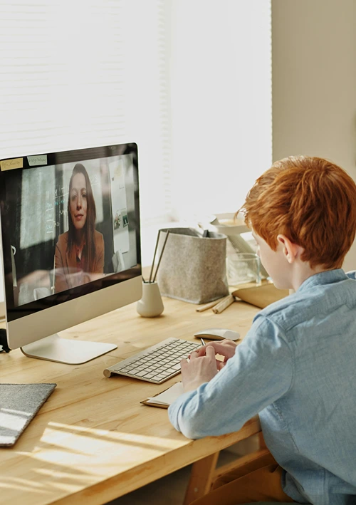 A teen student at desk interacting with online tutor on laptop.