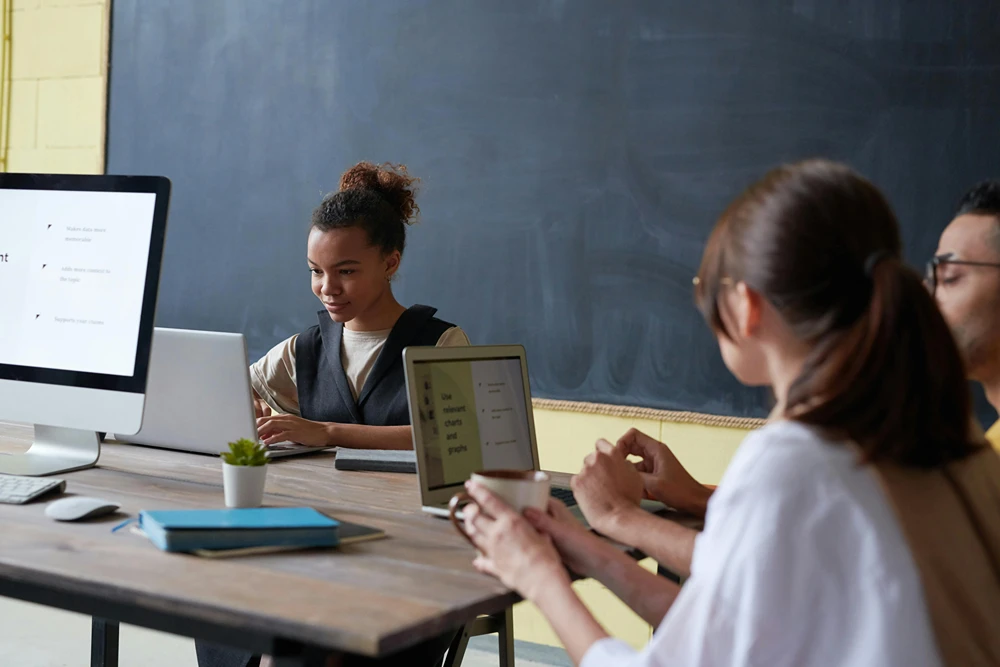 Groups of students with laptops working together at a table in class.
