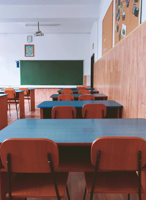 A row of empty desks in a classroom facing a green board.