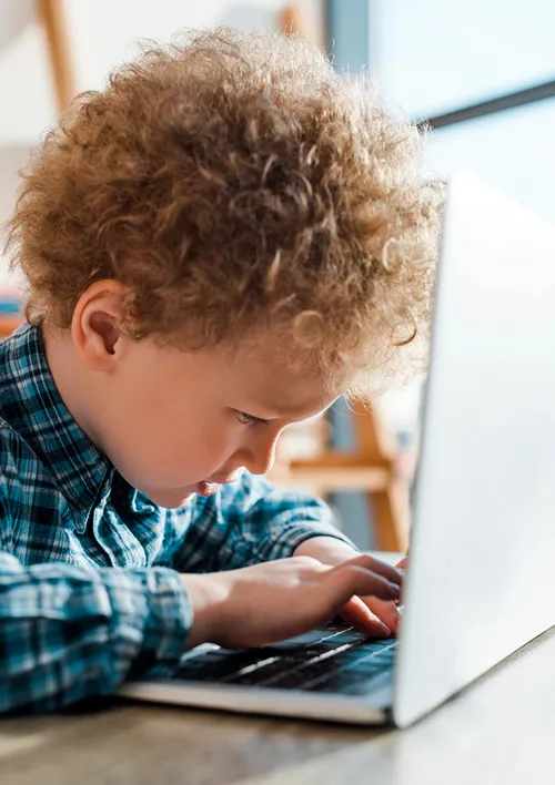Boy with eyes closely fixated on his fingers typing on laptop.