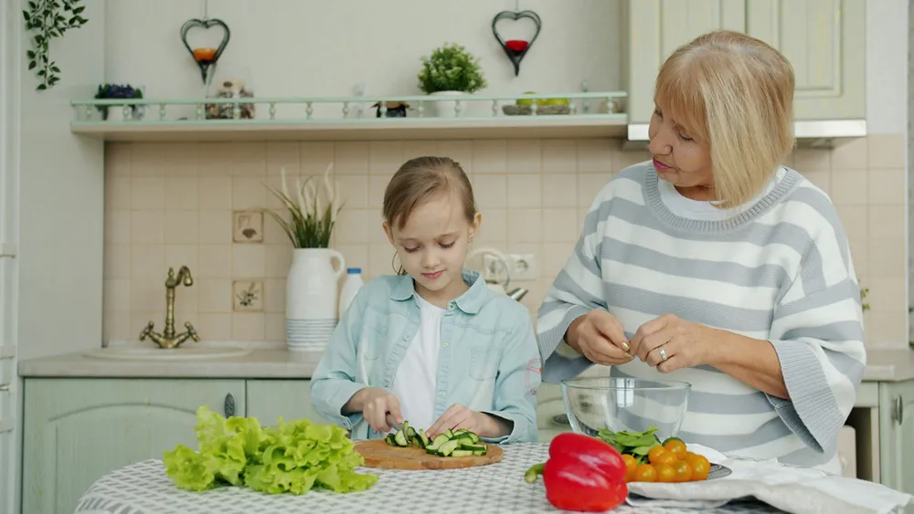 Grandmother and granddaughter prepare food in the kitchen.