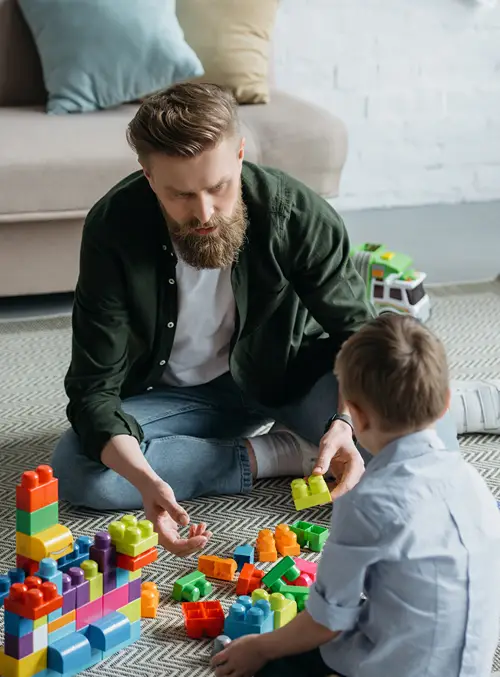 A dad is playing blocks on the living room floor with his son.