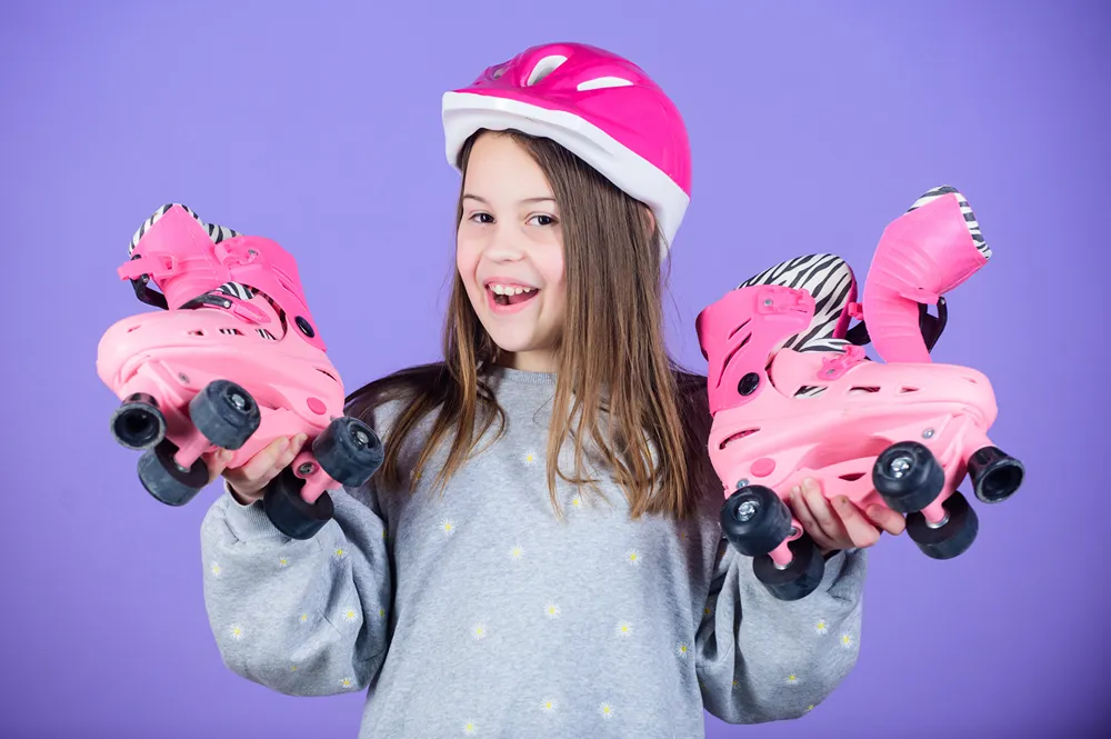 A tween girl is smiling as she holds up a pair of pink roller skates.