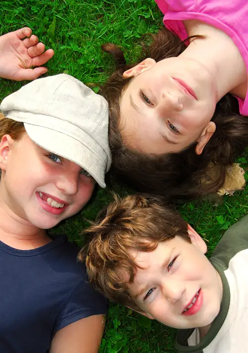 Happy siblings laying on grass looking up at camera.