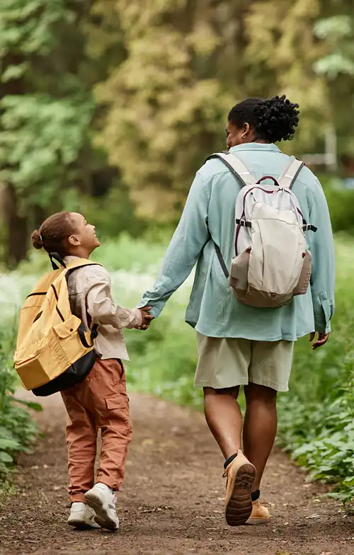 View from behind a mother and daughter with backpacks on a path.