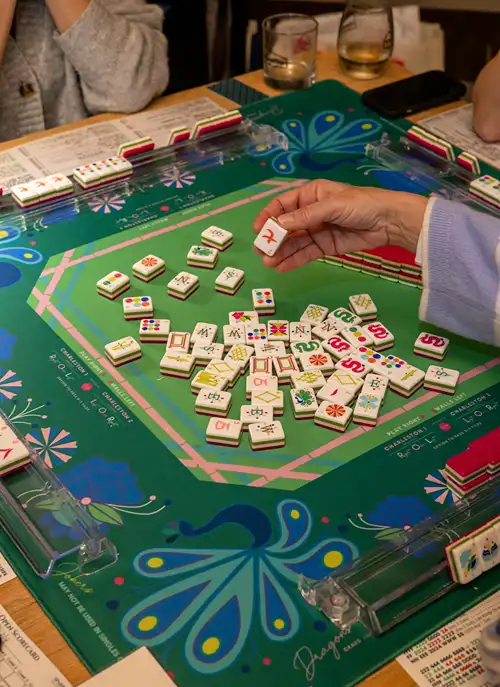 Adults gathered at a table playing Mahjong game.