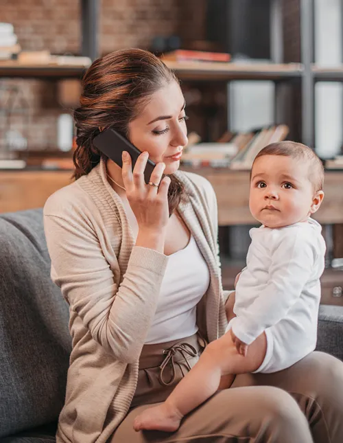Single mom on phone as baby sits on her lap.