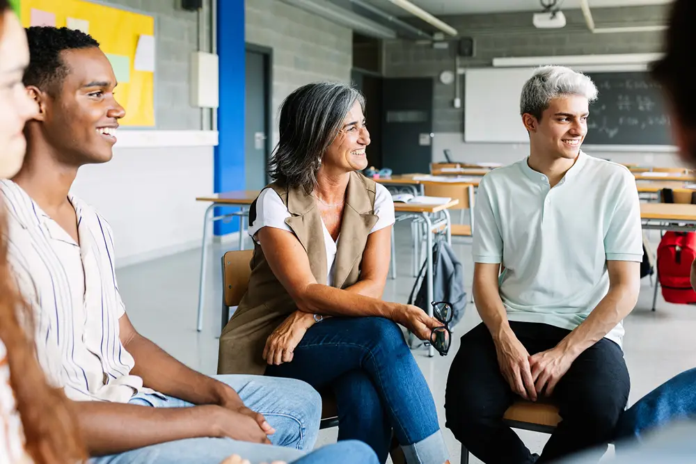 An older teacher with a group of adult students in casual classroom setting.