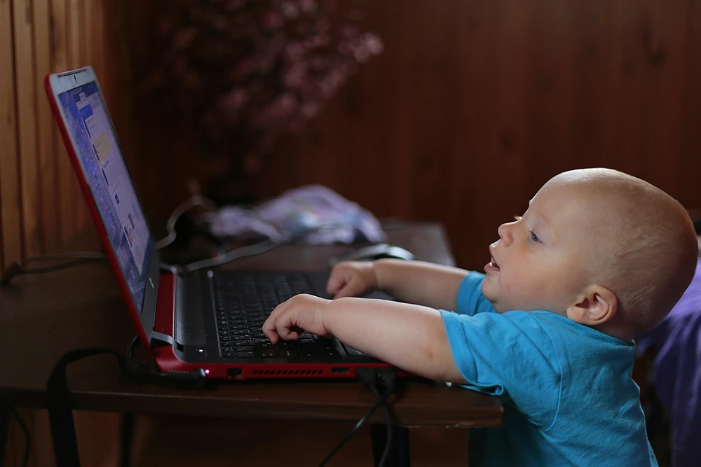 A baby can barely reach the keyboard of a laptop.