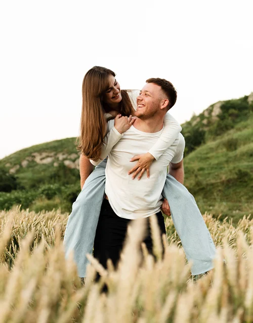 A woman on a man's back as he walked in a tall grassy field.