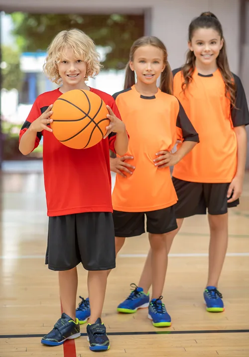 Boy holding a basketball on a court with two girls.