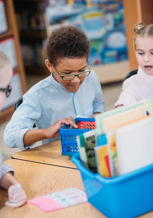 A boy looking through a box of learning materials in class.