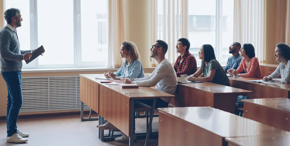 Hip teacher in front of small class of new college students.