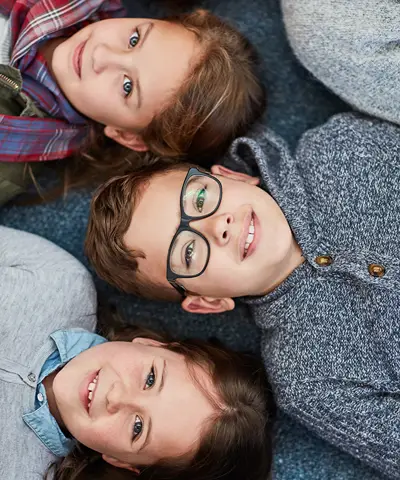Kids laying with backs on a floor looking up towards the ceiling.