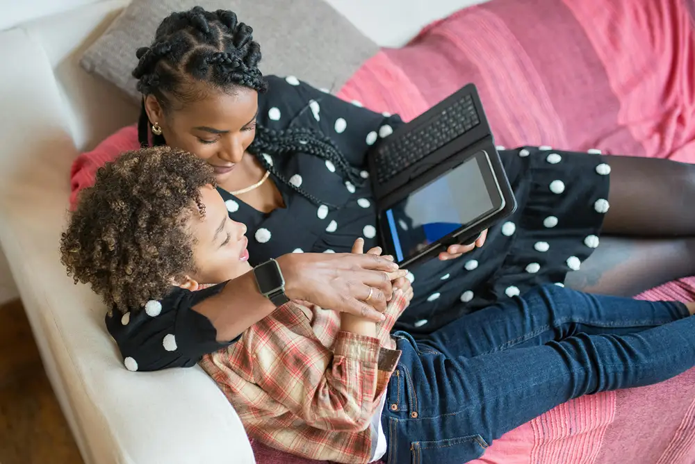A mother sits with her son as they use a tablet
