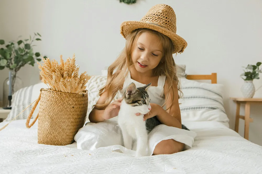 A little girl smiles as they plays with her cat on her bed.