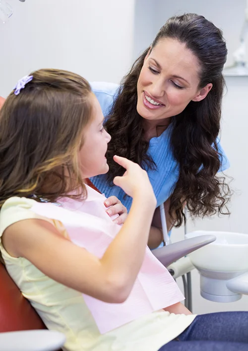 A female dentist smiles at a child in the dental chair.