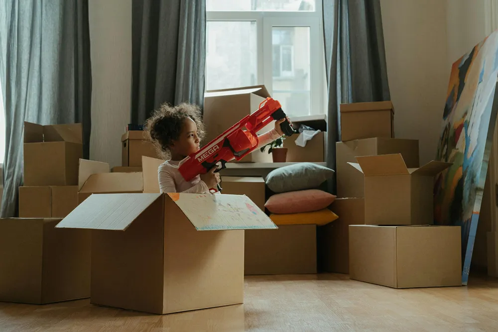 A girl sits in a cardboard box shooting a nerf gun.