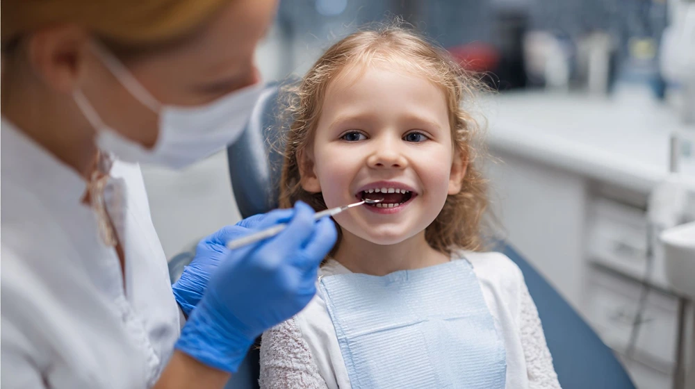 Dentist puts a dental instrument into a little girl's mouth.