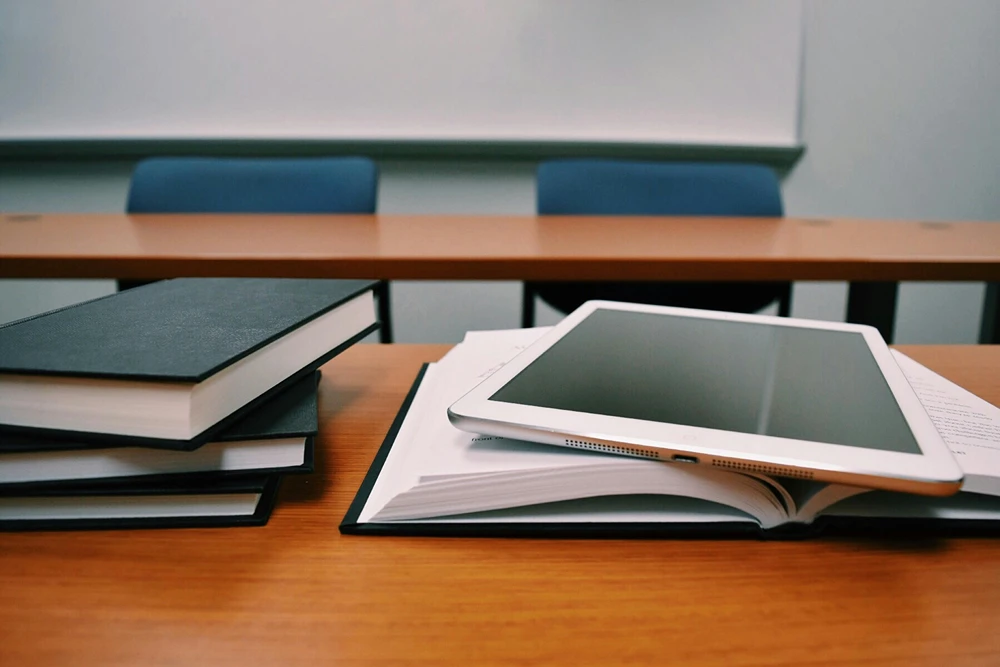 A desk in a lecture hall with a tablet and books on a table.