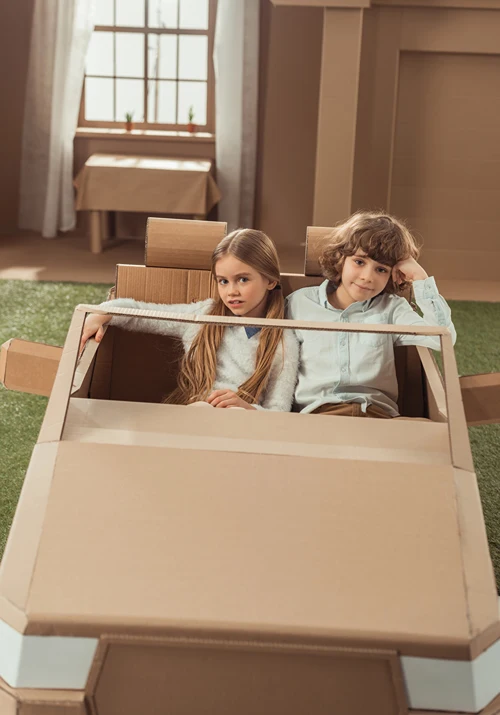 Boy and girl playing in a carboard box cut to look like a car.