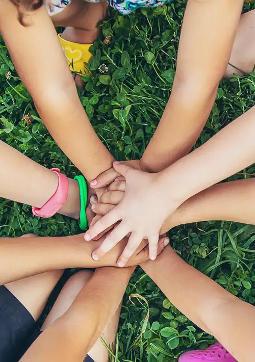 Kids kneeling down in a circle and stacking their hands together on the grass