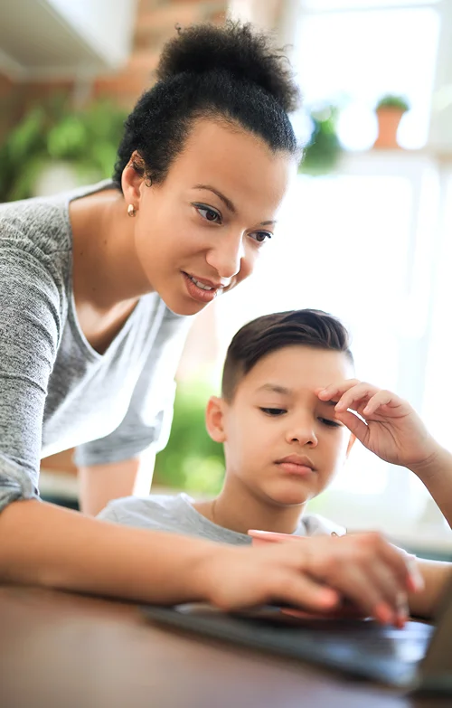 A mother is teaching her son how to use a lap top.