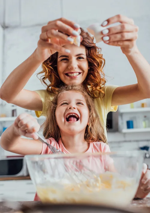 Mother and daughter laughing as they crack an egg in the kitchen.