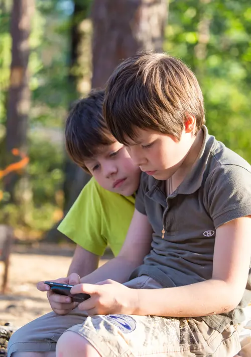 Two boys sitting outdoors and looking at a smartphone.